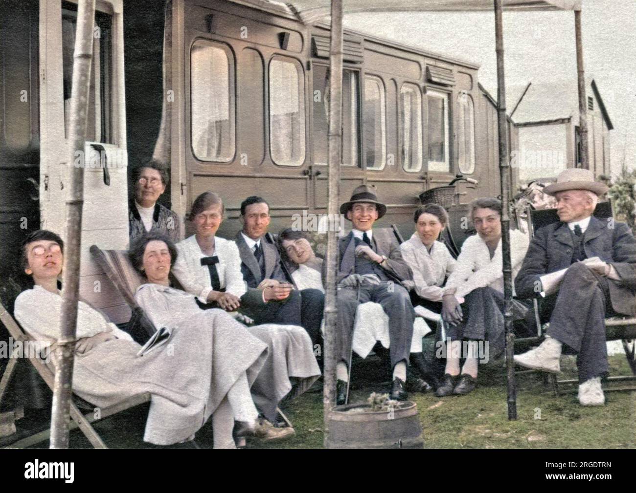 Un grande gruppo di vacanzieri seduti di fronte ad una carovana che sembra essere stata adattata da una vecchia carrozza ferroviaria. Foto Stock