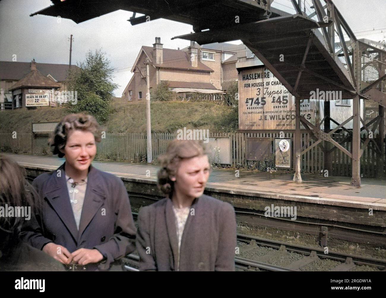 Due giovani donne in una stazione ferroviaria nel sud di Londra. Una pubblicità sulla piattaforma opposta è per proprietà, case di carattere per ú745 freehold. Un altro cartello pubblicizza appartamenti indipendenti da affittare. Foto Stock