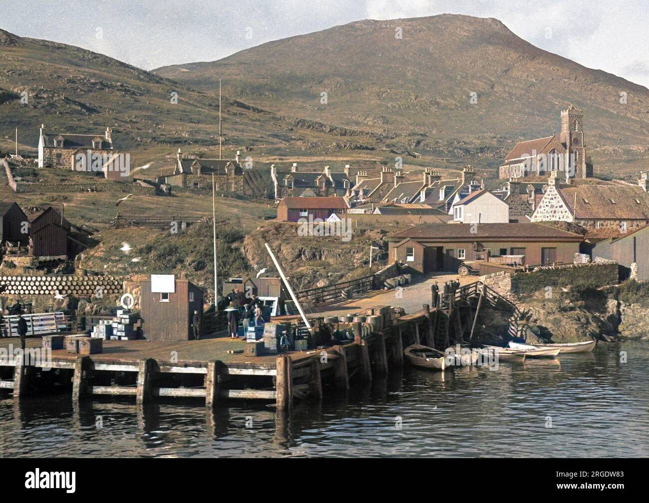 Una scena sul mare in Scozia con un molo, case e una chiesa. Barili possono essere visti accumulati su sulla sinistra. Foto Stock