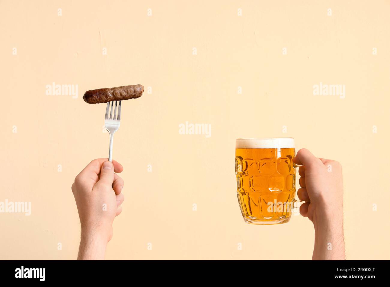 Uomo con un bicchiere di birra e salsiccia su sfondo beige Foto Stock