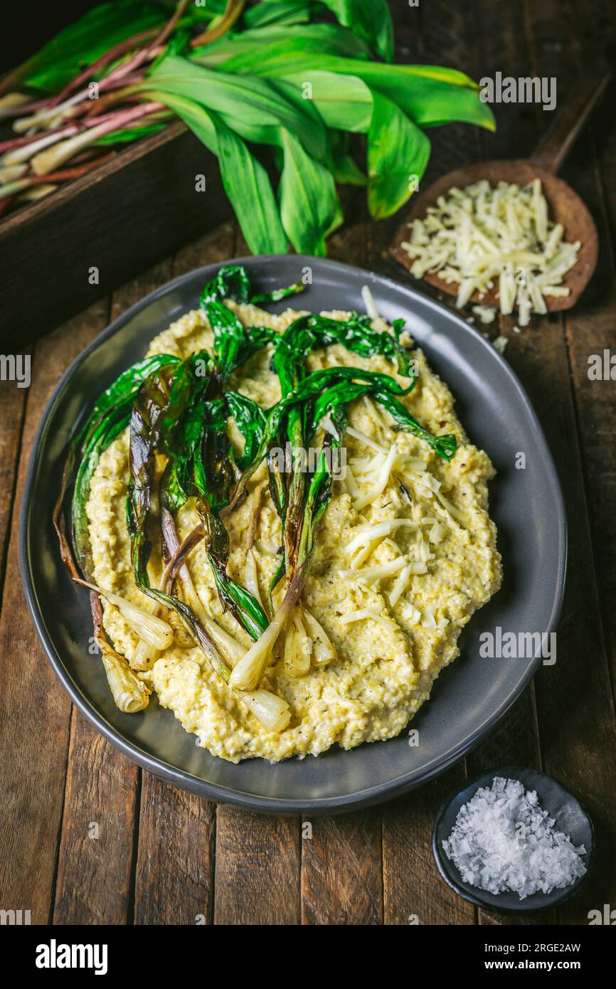 Polenta e rampe grigliate su un piatto con rampe fresche e formaggio grattugiato sullo sfondo Foto Stock