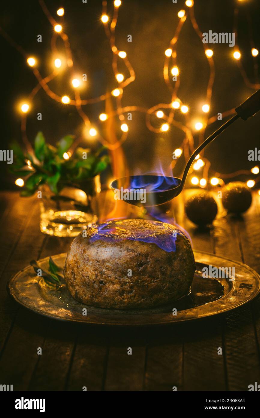 Budino di Natale con cucchiaio e pappagallo su piatto di peltro con holly e luci di Natale Foto Stock