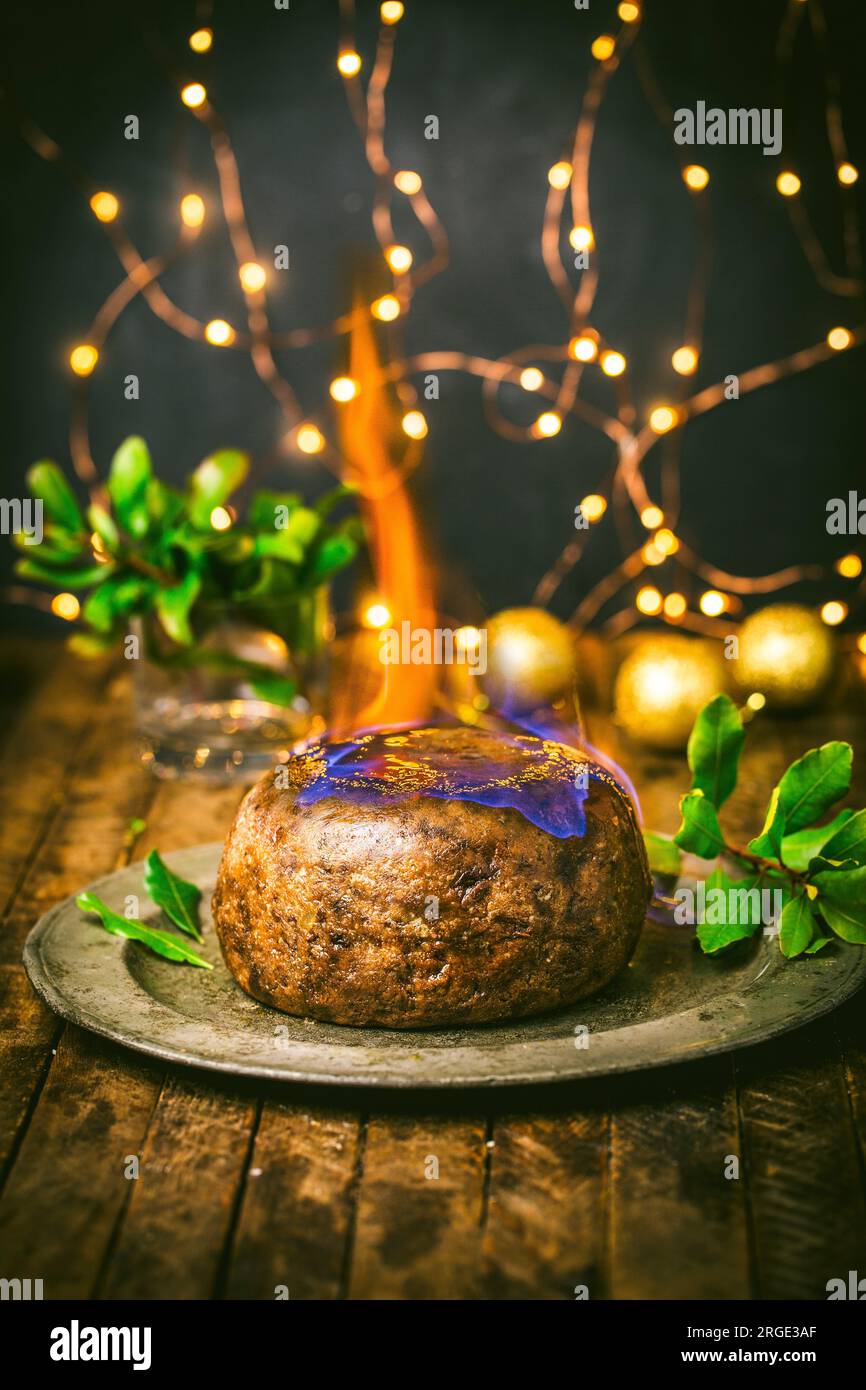 Budino di Natale con fiamma su piatto di peltro con holly e luci di Natale Foto Stock