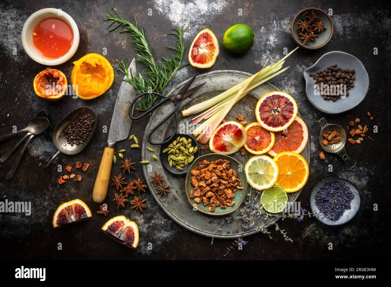 Disposizione piatta di fette di agrumi colorate, succhi di frutta, citronella, erbe e spezie su sfondo scuro. Ingredienti per acqua tonica fatta in casa Foto Stock