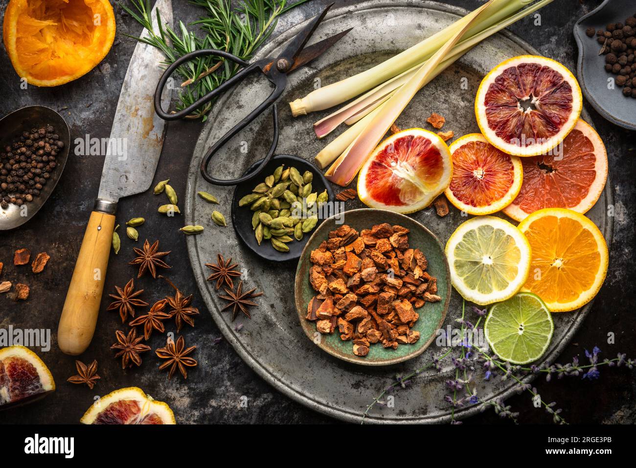 Disposizione piatta di fette di agrumi colorate, succhi di frutta, citronella, erbe e spezie su sfondo scuro. Ingredienti per acqua tonica fatta in casa Foto Stock