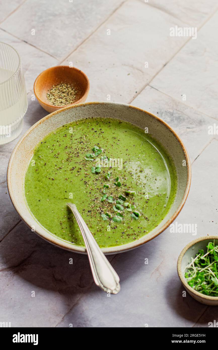 ciotola di zuppa di verdure verde con cucchiaio, guarnita con pepe nero e crescione Foto Stock