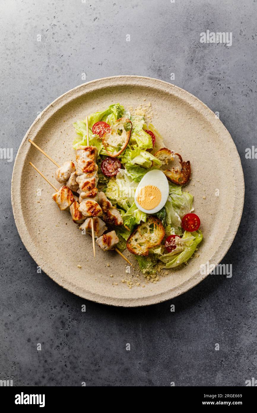 Insalata Caesar con petto di pollo su spiedini e uovo su piatto Foto Stock