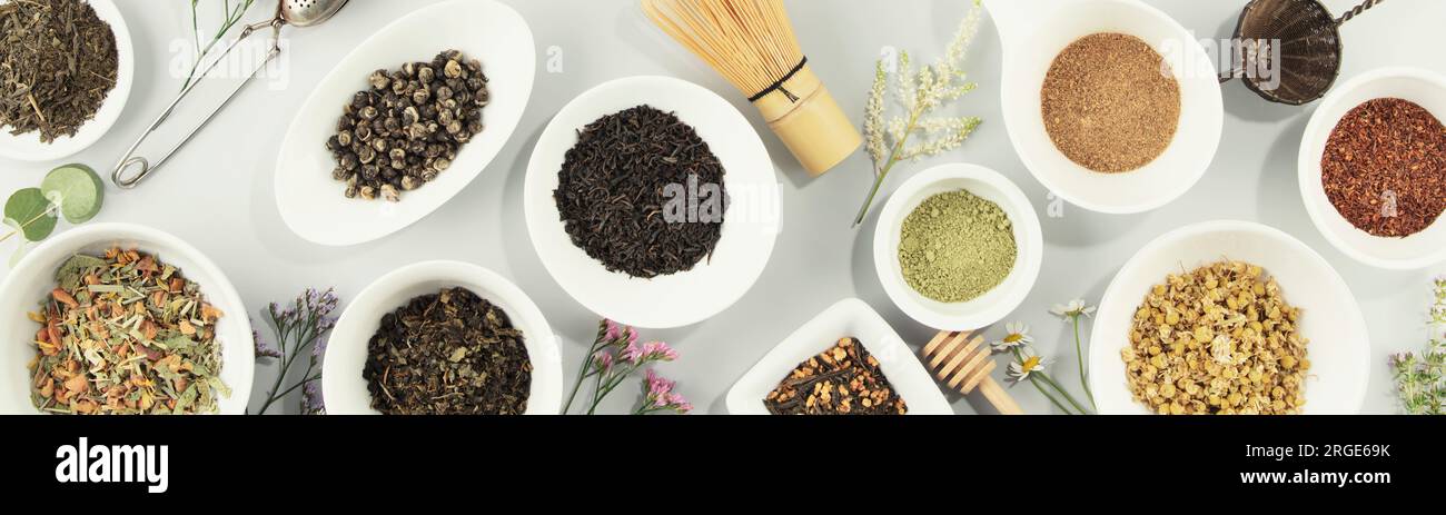 Assortimento di tè secco in ciotole in ceramica bianca. Matcha, rooibos, nero, verde, miscela di erbe, masala e tè camomilla. Vista dall'alto, base piatta, banner Foto Stock