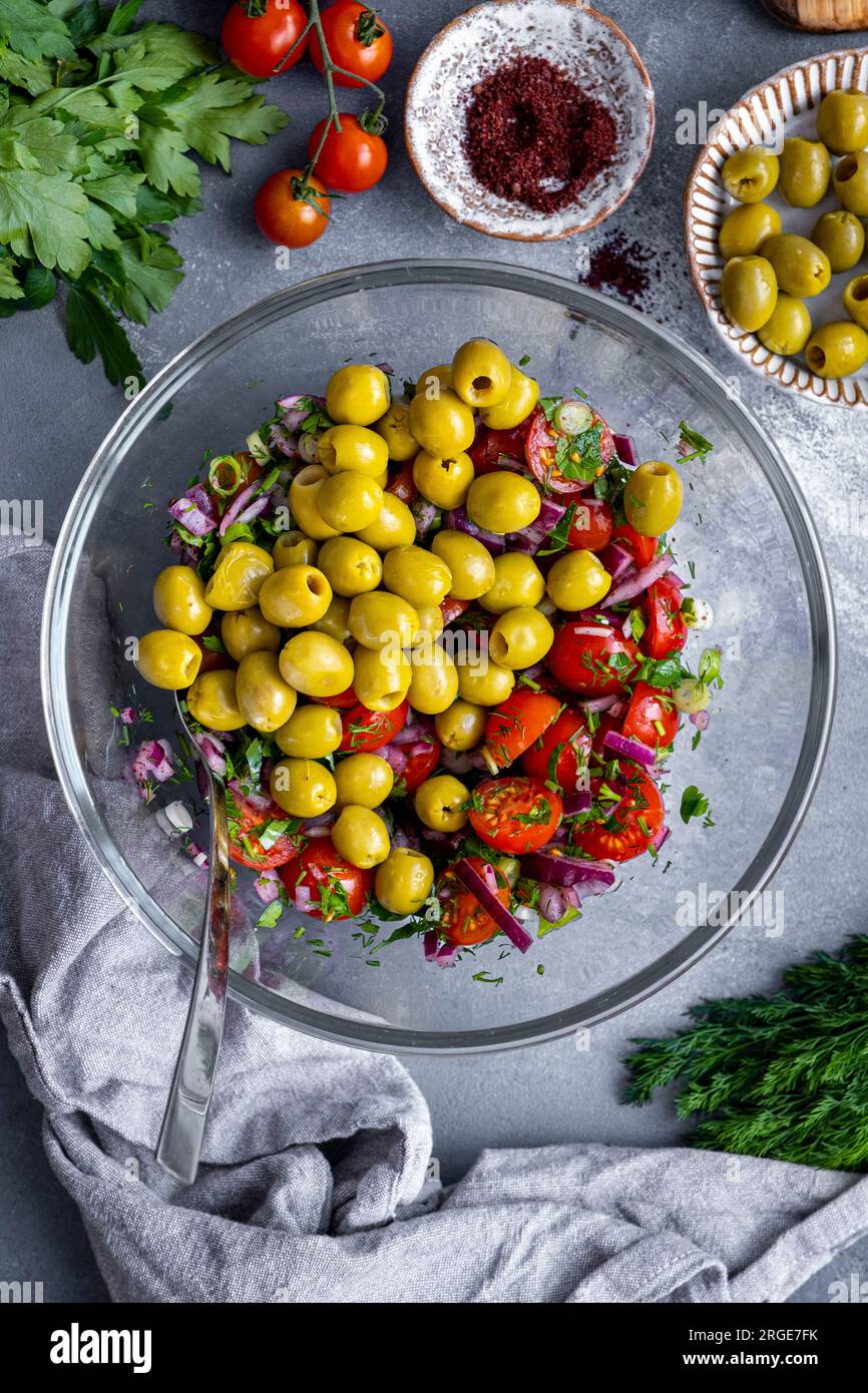 Cipolle tritate, cipolle verdi, prezzemolo, aneto, pomodori ciliegini tagliati a metà e olive verdi snocciolate in un recipiente di vetro. Foto Stock