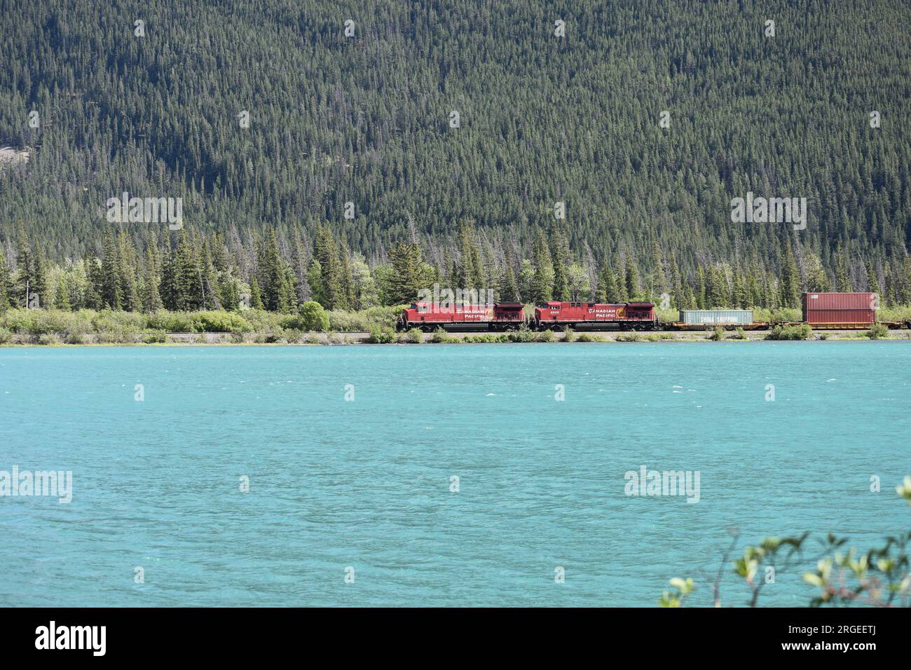 Treno Canadian Pacific che attraversa le Montagne Rocciose canadesi lungo le acque cristalline del lago Gap, Alberta. Foto Stock