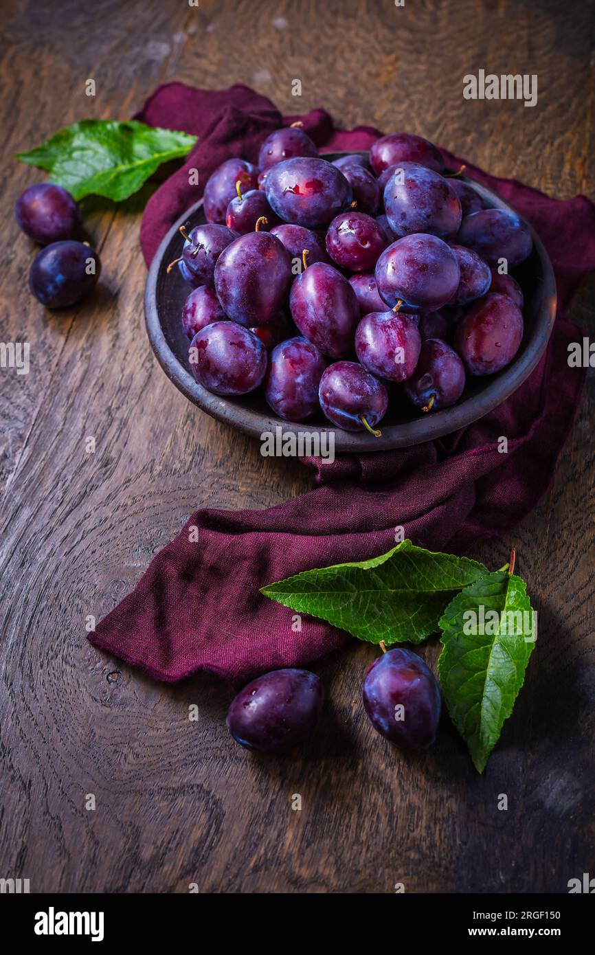 Prugne fresche sul piatto su sfondo di legno scuro Foto Stock