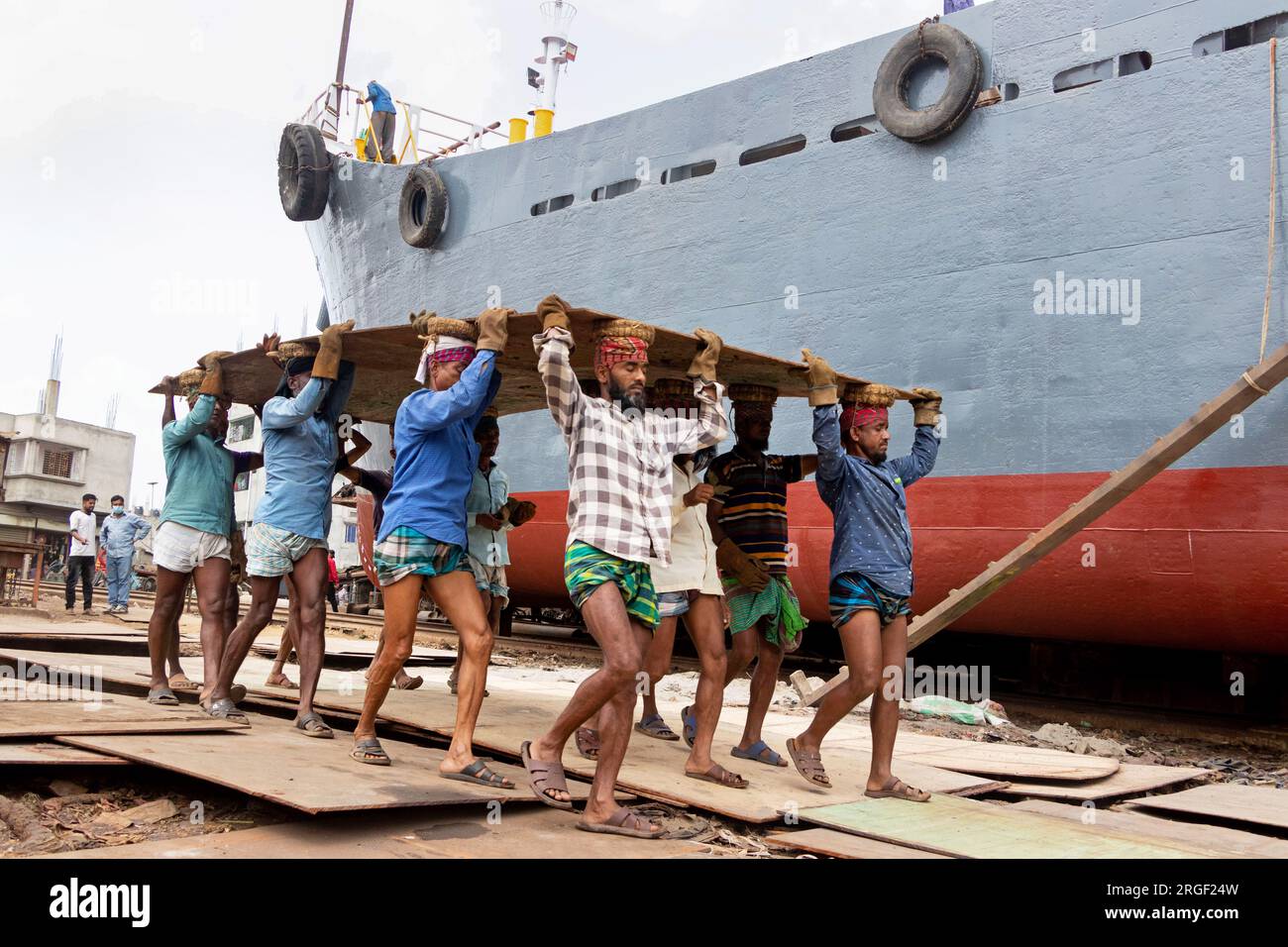 Dhaka, Dhaka, Bangladesh. 9 agosto 2023. Un gruppo di portatori trasporta una pesante piastra di acciaio di 250 kg in un cantiere navale sulla riva del fiume Buriganga, a Keraniganj, vicino a Dacca, Bangladesh. Dozzine di cantieri che occupano 30,96 acri della costa di Buriganga sono stati in funzione negli ultimi 50 anni. Viene utilizzato principalmente per riparare e riparare vecchie navi e costruire nuove navi. Le maestranze lavorano nel cantiere senza caschi, maschere facciali o scarpe di sicurezza. Lavorano sodo tutto il giorno, ma sono ancora pagati salari minimi. Con un numero crescente di ordini da parte di acquirenti sia locali che globali, il cantieristico Foto Stock
