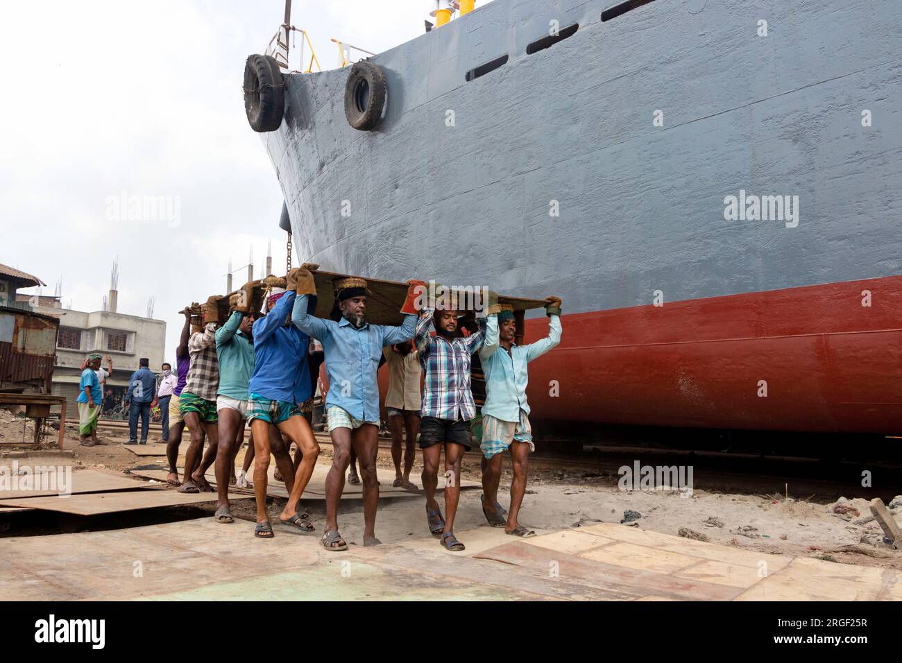 Dhaka, Dhaka, Bangladesh. 9 agosto 2023. Un gruppo di portatori trasporta una pesante piastra di acciaio di 250 kg in un cantiere navale sulla riva del fiume Buriganga, a Keraniganj, vicino a Dacca, Bangladesh. Dozzine di cantieri che occupano 30,96 acri della costa di Buriganga sono stati in funzione negli ultimi 50 anni. Viene utilizzato principalmente per riparare e riparare vecchie navi e costruire nuove navi. Le maestranze lavorano nel cantiere senza caschi, maschere facciali o scarpe di sicurezza. Lavorano sodo tutto il giorno, ma sono ancora pagati salari minimi. Con un numero crescente di ordini da parte di acquirenti sia locali che globali, il cantieristico Foto Stock