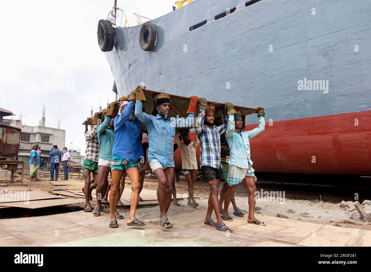 Dhaka, Dhaka, Bangladesh. 9 agosto 2023. Un gruppo di portatori trasporta una pesante piastra di acciaio di 250 kg in un cantiere navale sulla riva del fiume Buriganga, a Keraniganj, vicino a Dacca, Bangladesh. Dozzine di cantieri che occupano 30,96 acri della costa di Buriganga sono stati in funzione negli ultimi 50 anni. Viene utilizzato principalmente per riparare e riparare vecchie navi e costruire nuove navi. Le maestranze lavorano nel cantiere senza caschi, maschere facciali o scarpe di sicurezza. Lavorano sodo tutto il giorno, ma sono ancora pagati salari minimi. Con un numero crescente di ordini da parte di acquirenti sia locali che globali, il cantieristico Foto Stock