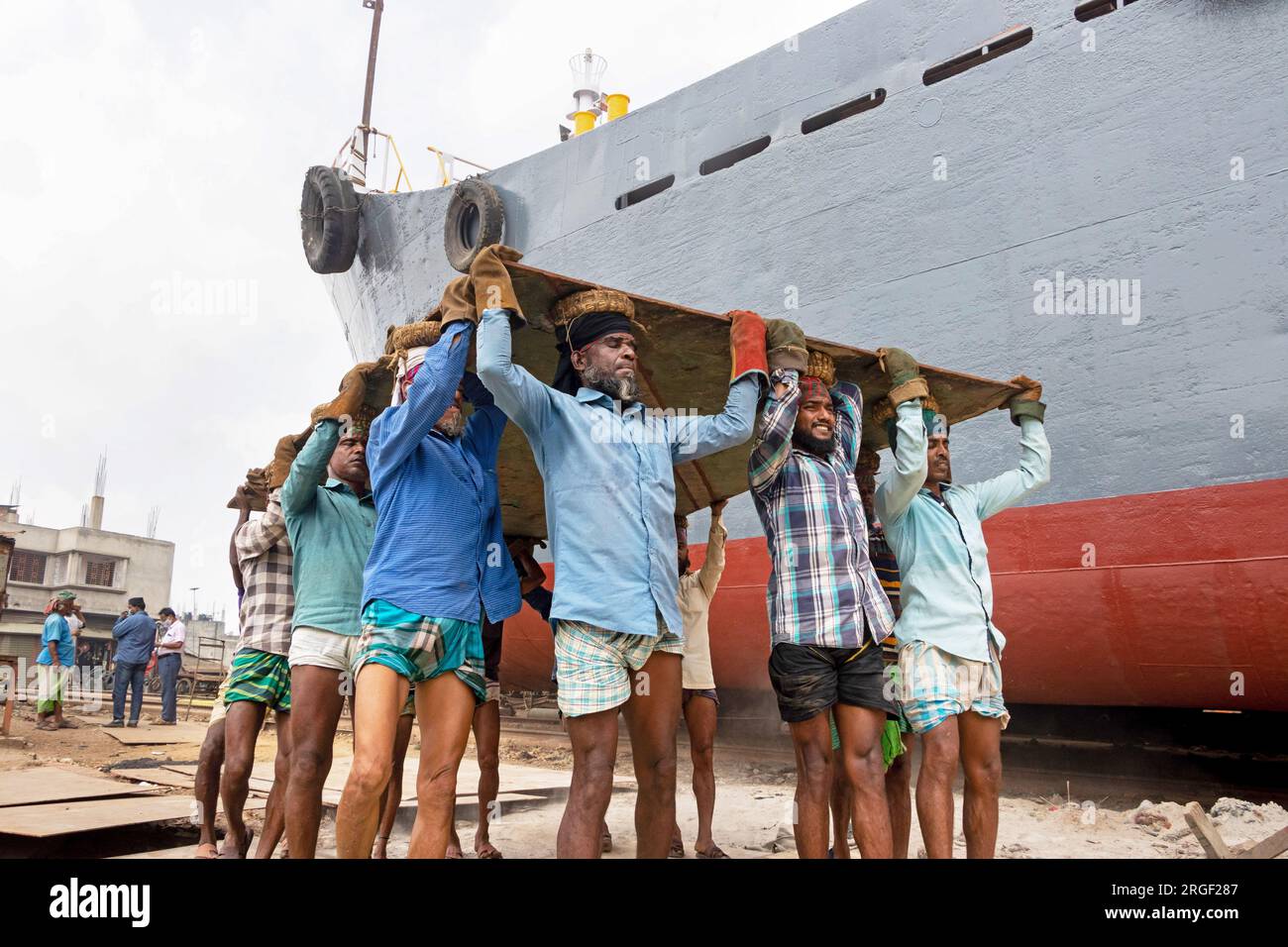 Dhaka, Dhaka, Bangladesh. 9 agosto 2023. Un gruppo di portatori trasporta una pesante piastra di acciaio di 250 kg in un cantiere navale sulla riva del fiume Buriganga, a Keraniganj, vicino a Dacca, Bangladesh. Dozzine di cantieri che occupano 30,96 acri della costa di Buriganga sono stati in funzione negli ultimi 50 anni. Viene utilizzato principalmente per riparare e riparare vecchie navi e costruire nuove navi. Le maestranze lavorano nel cantiere senza caschi, maschere facciali o scarpe di sicurezza. Lavorano sodo tutto il giorno, ma sono ancora pagati salari minimi. Con un numero crescente di ordini da parte di acquirenti sia locali che globali, il cantieristico Foto Stock