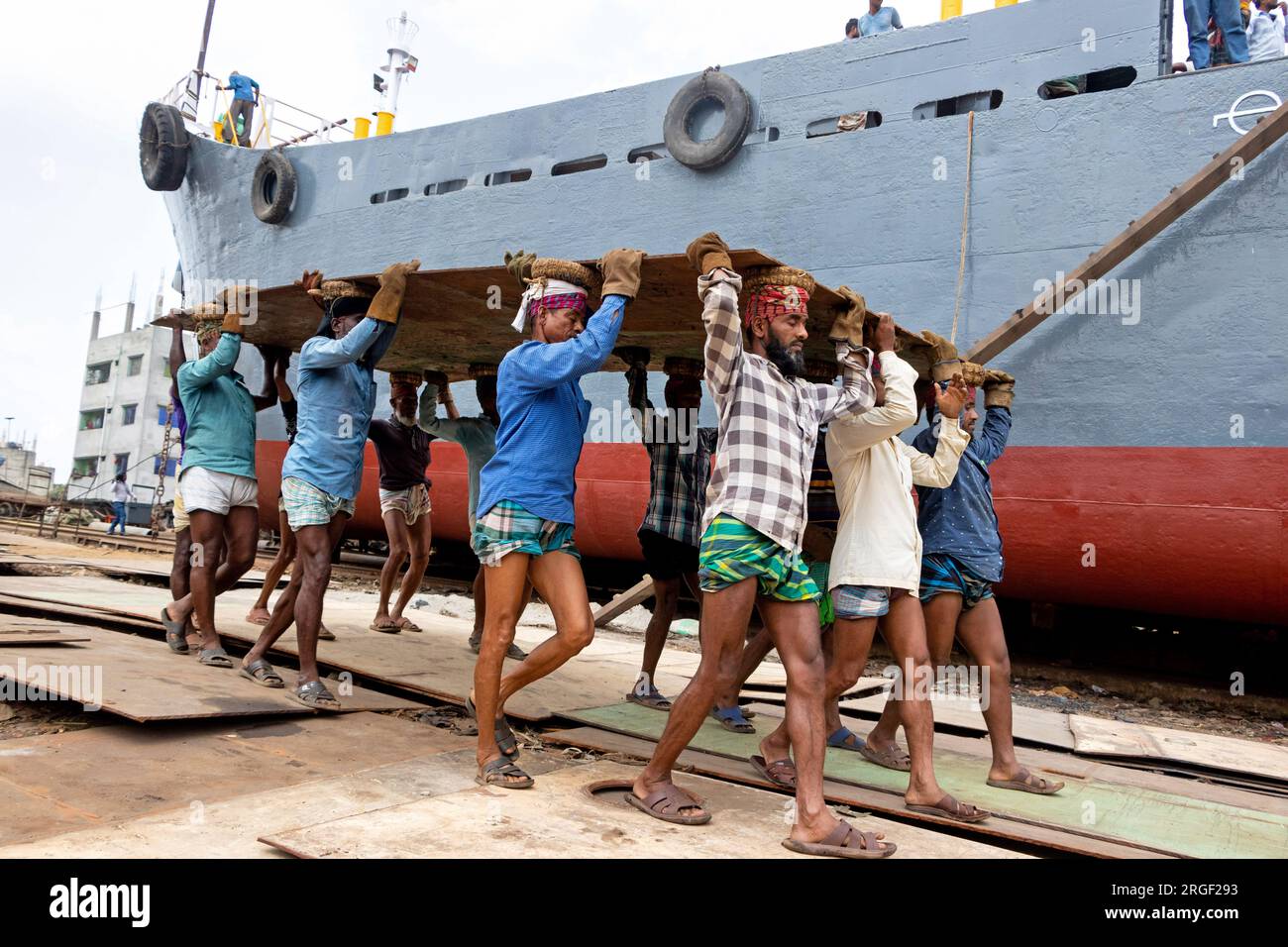Dhaka, Dhaka, Bangladesh. 9 agosto 2023. Un gruppo di portatori trasporta una pesante piastra di acciaio di 250 kg in un cantiere navale sulla riva del fiume Buriganga, a Keraniganj, vicino a Dacca, Bangladesh. Dozzine di cantieri che occupano 30,96 acri della costa di Buriganga sono stati in funzione negli ultimi 50 anni. Viene utilizzato principalmente per riparare e riparare vecchie navi e costruire nuove navi. Le maestranze lavorano nel cantiere senza caschi, maschere facciali o scarpe di sicurezza. Lavorano sodo tutto il giorno, ma sono ancora pagati salari minimi. Con un numero crescente di ordini da parte di acquirenti sia locali che globali, il cantieristico Foto Stock