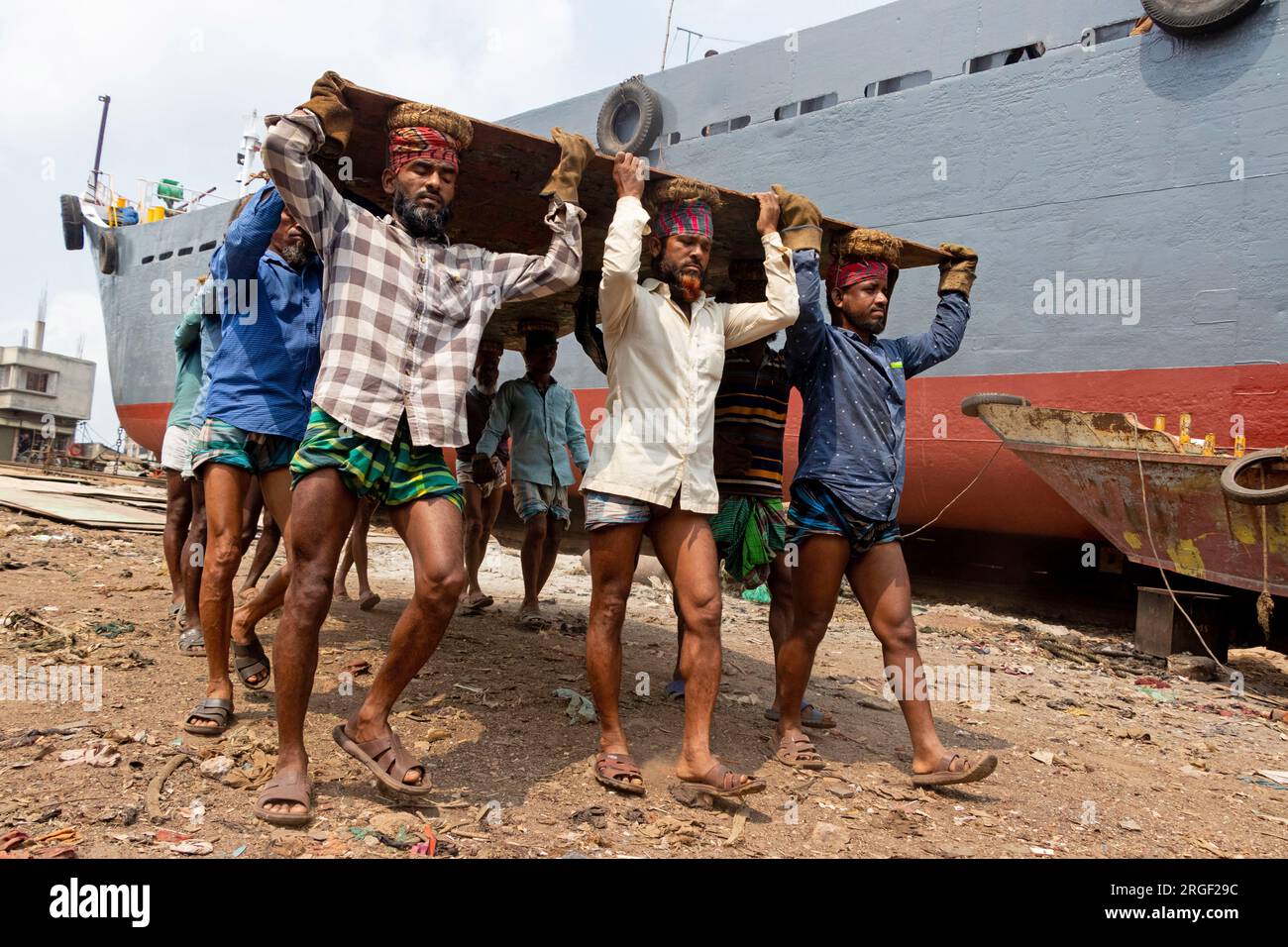 Dhaka, Dhaka, Bangladesh. 9 agosto 2023. Un gruppo di portatori trasporta una pesante piastra di acciaio di 250 kg in un cantiere navale sulla riva del fiume Buriganga, a Keraniganj, vicino a Dacca, Bangladesh. Dozzine di cantieri che occupano 30,96 acri della costa di Buriganga sono stati in funzione negli ultimi 50 anni. Viene utilizzato principalmente per riparare e riparare vecchie navi e costruire nuove navi. Le maestranze lavorano nel cantiere senza caschi, maschere facciali o scarpe di sicurezza. Lavorano sodo tutto il giorno, ma sono ancora pagati salari minimi. Con un numero crescente di ordini da parte di acquirenti sia locali che globali, il cantieristico Foto Stock