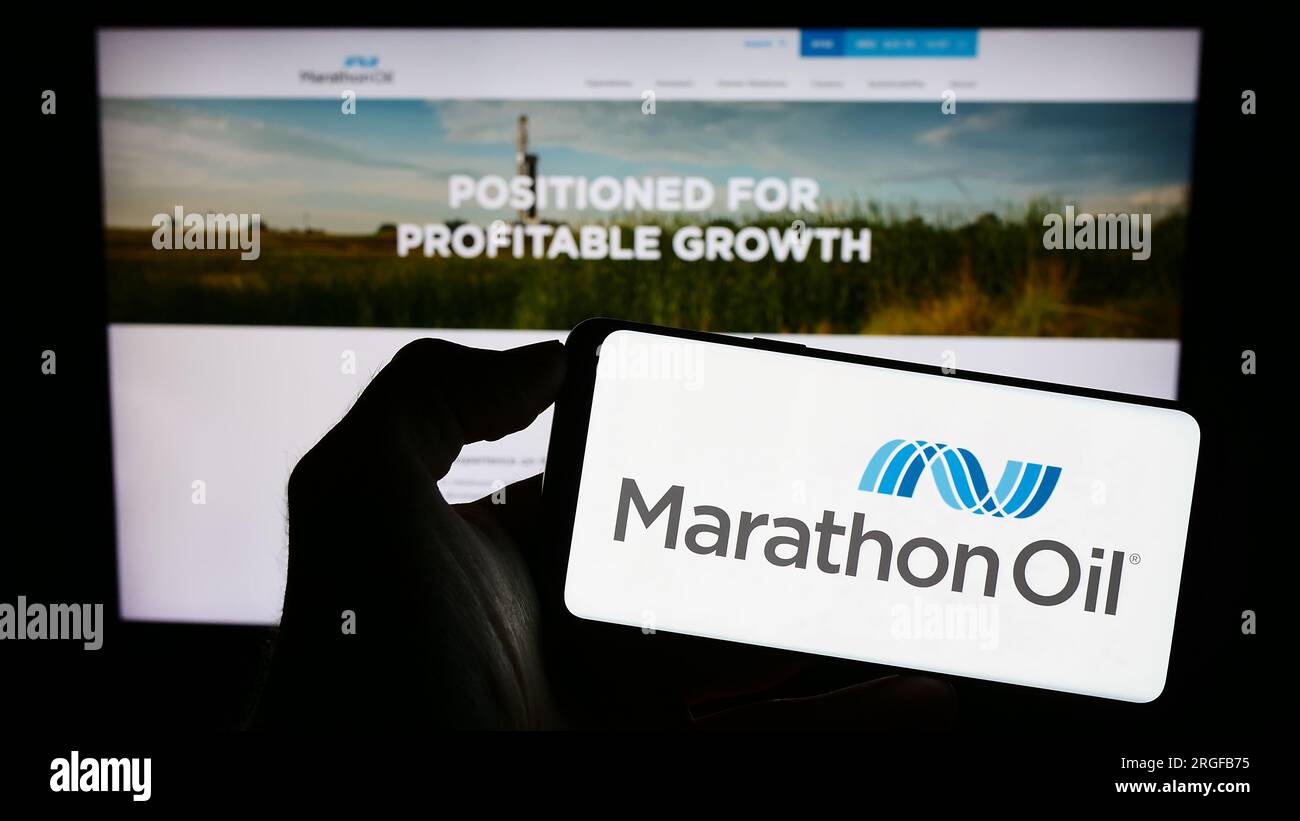 Persona in possesso di un cellulare con il logo della società petrolifera americana Marathon Oil Corporation sullo schermo davanti alla pagina Web. Concentrarsi sul display del telefono. Foto Stock