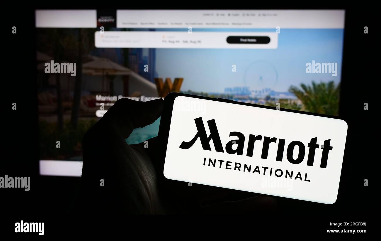 Persona in possesso di un cellulare con il logo della società alberghiera americana Marriott International Inc. Sullo schermo davanti alla pagina Web. Concentrarsi sul display del telefono. Foto Stock