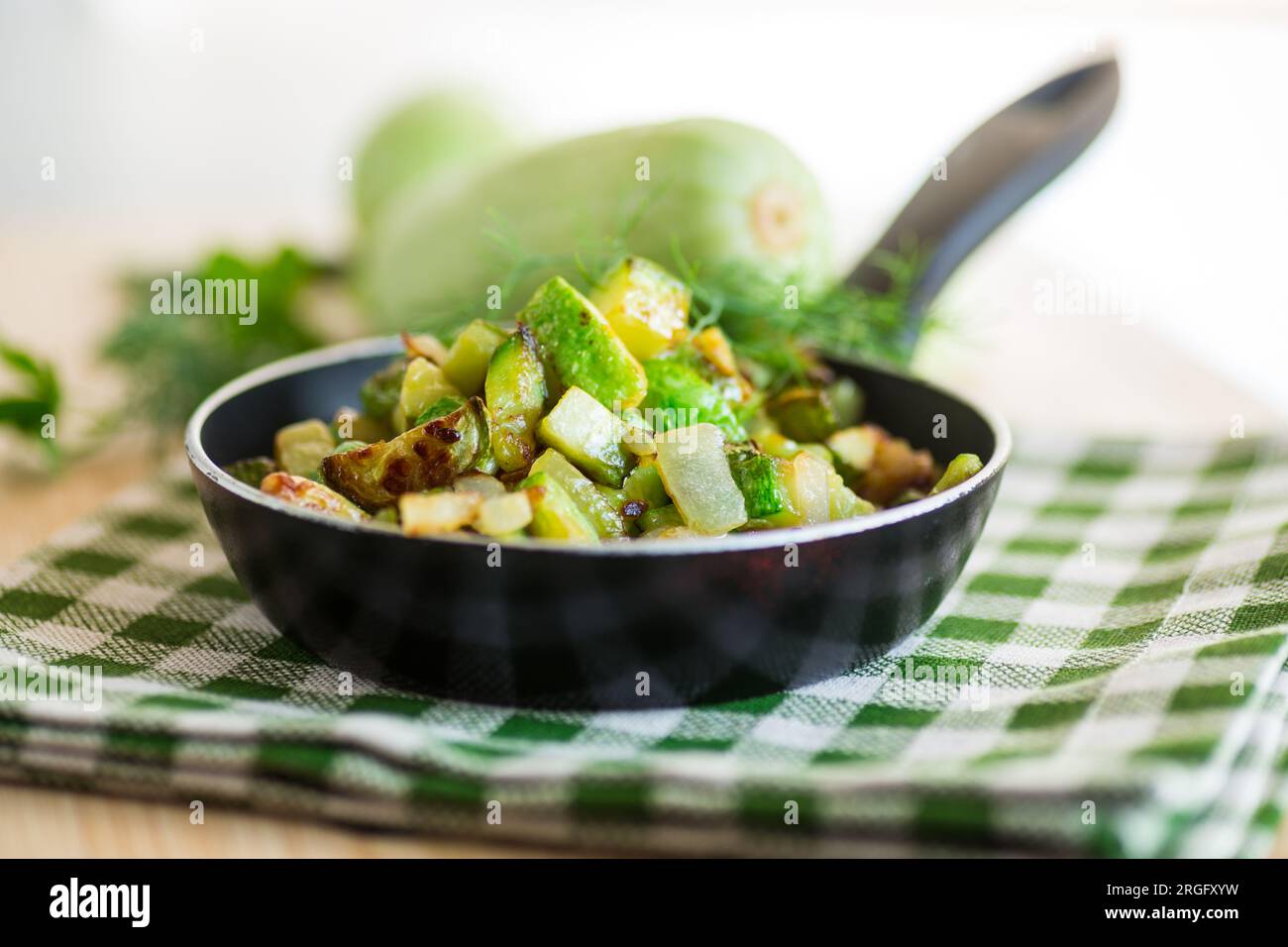 Zucchine a fette fritte con cipolle ed erbe in una padella su un tavolo di legno. Foto Stock