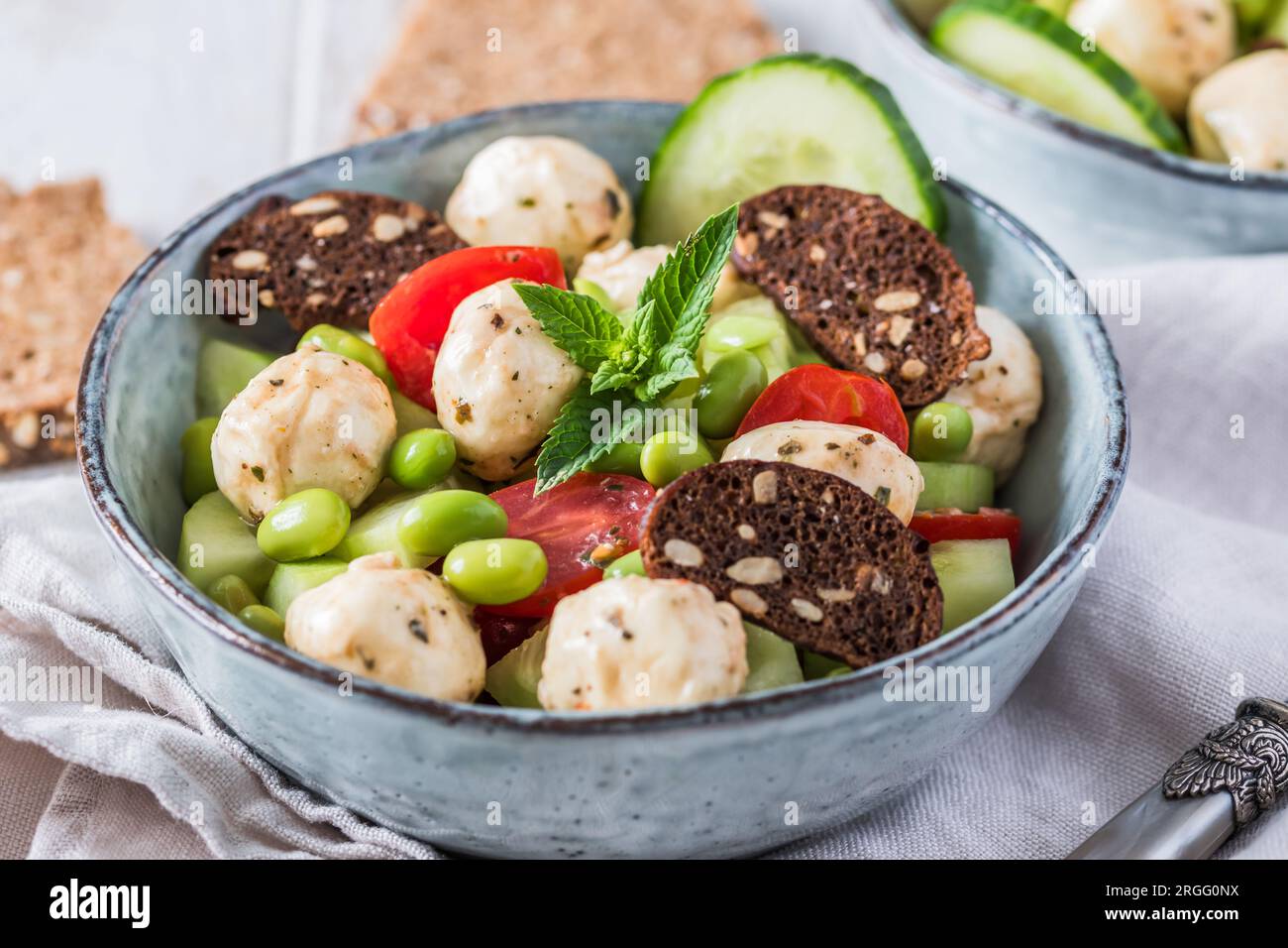 Insalata estiva con cetrioli, mini pomodori, mini mozzarella e soia su fondo di legno bianco Foto Stock