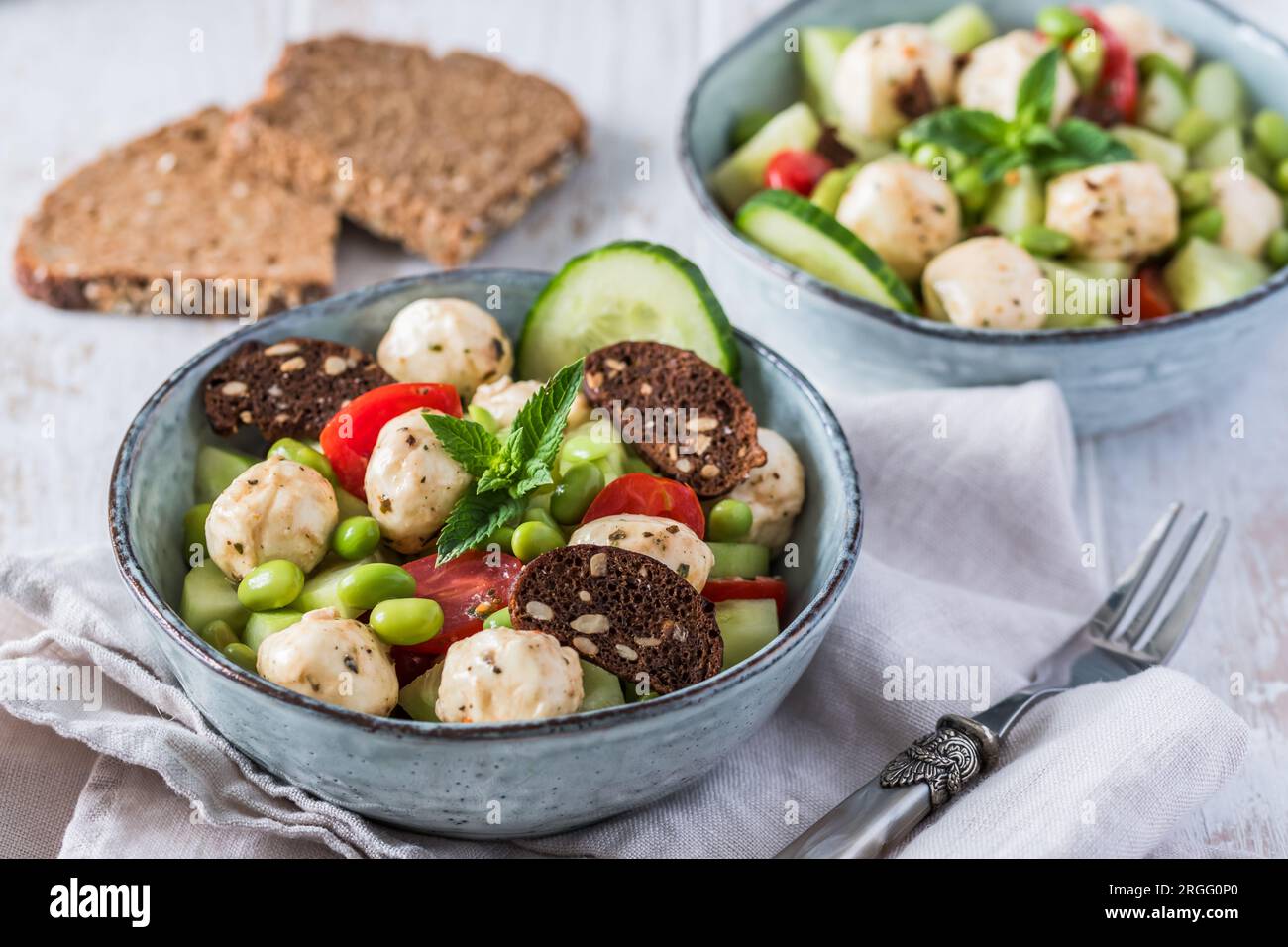 Insalata estiva con cetrioli, mini pomodori, mini mozzarella e soia su fondo di legno bianco Foto Stock