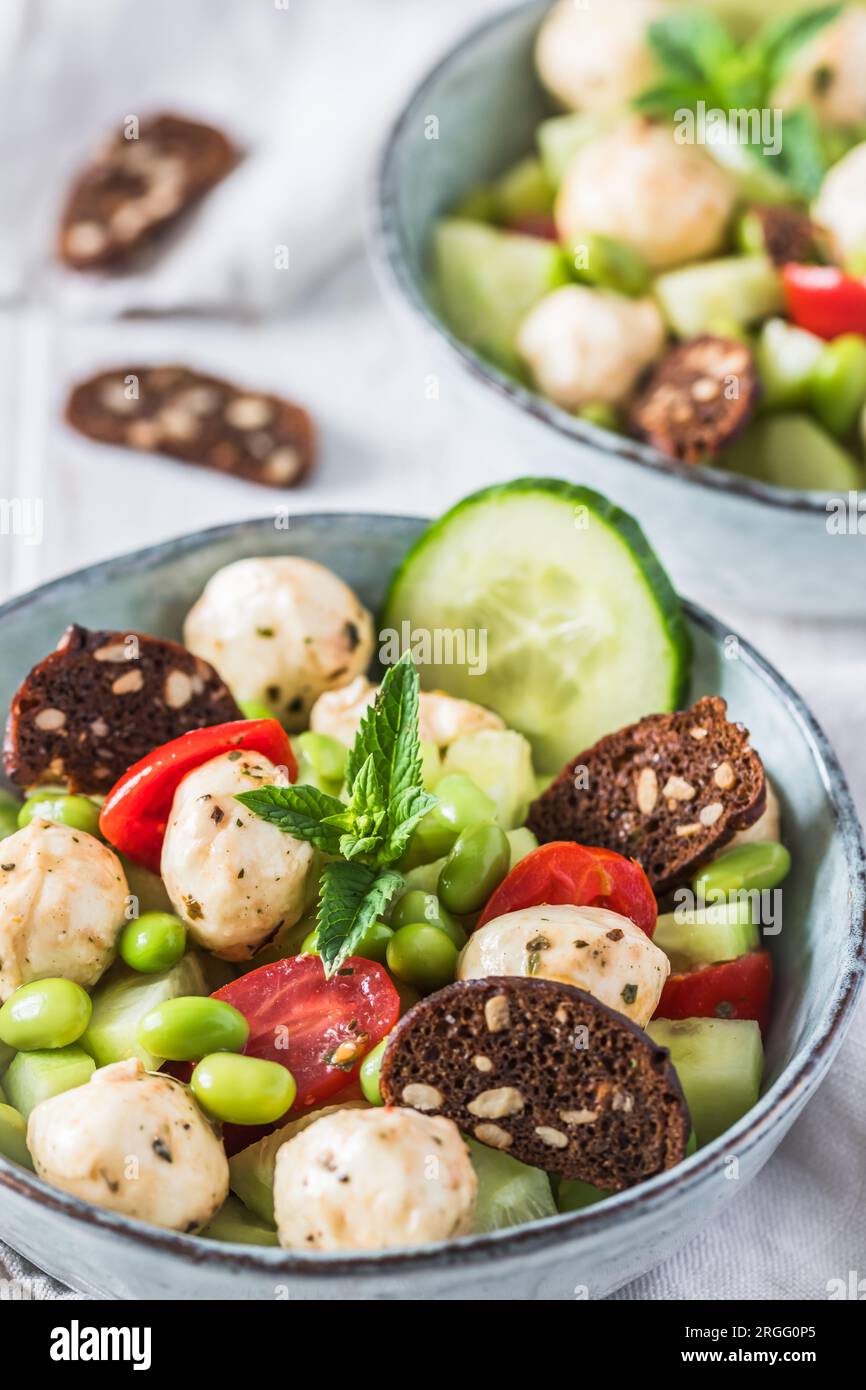 Insalata estiva con cetrioli, mini tomati, mini mozzarella e soia su fondo di legno bianco, verticale Foto Stock