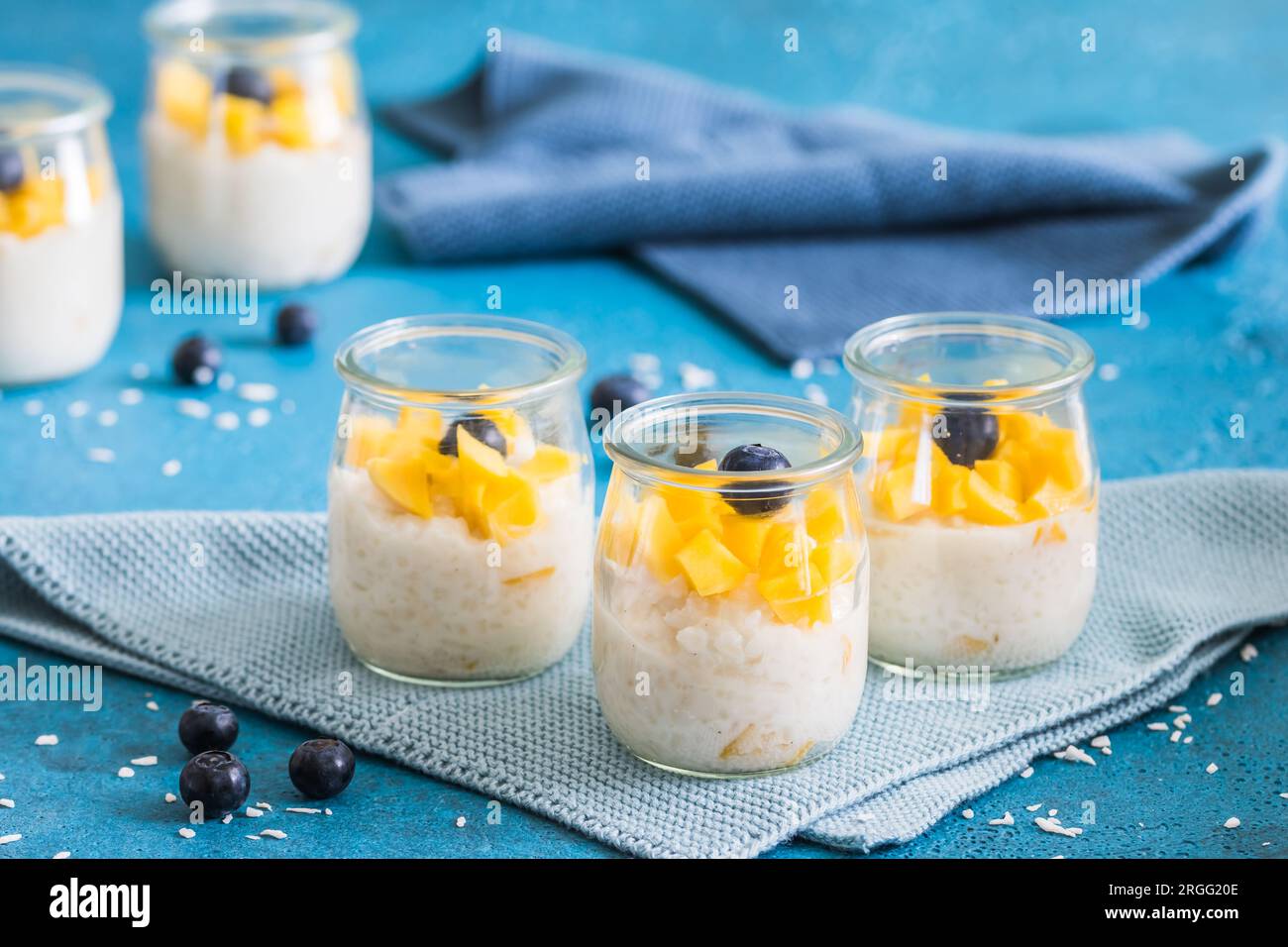 Budino di riso al cocco con mango in bicchieri da dessert su sfondo blu Foto Stock
