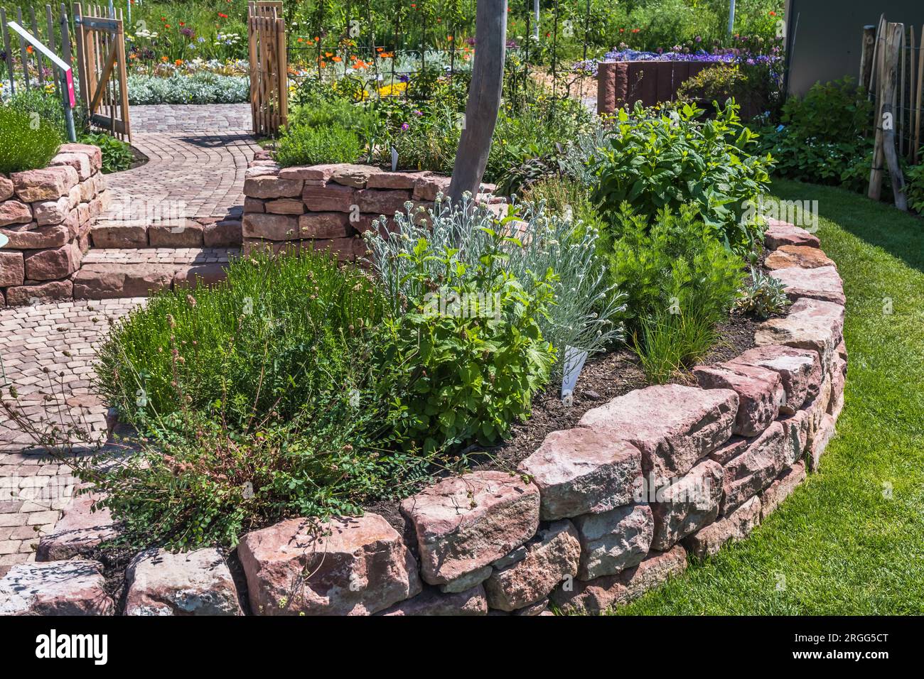 Giardino con parete in arenaria, sentiero pavimentato, patio e letto alle erbe Foto Stock