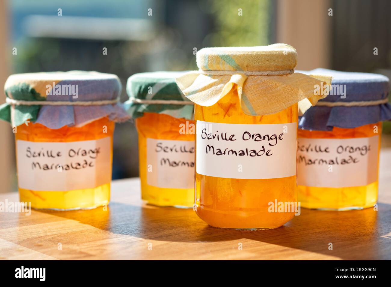 Un gruppo di barattoli contenenti marmellata d'arancia di Siviglia fatta in casa. Le vaschette hanno etichette scritte a mano e rivestimenti in tessuto sopra i coperchi Foto Stock