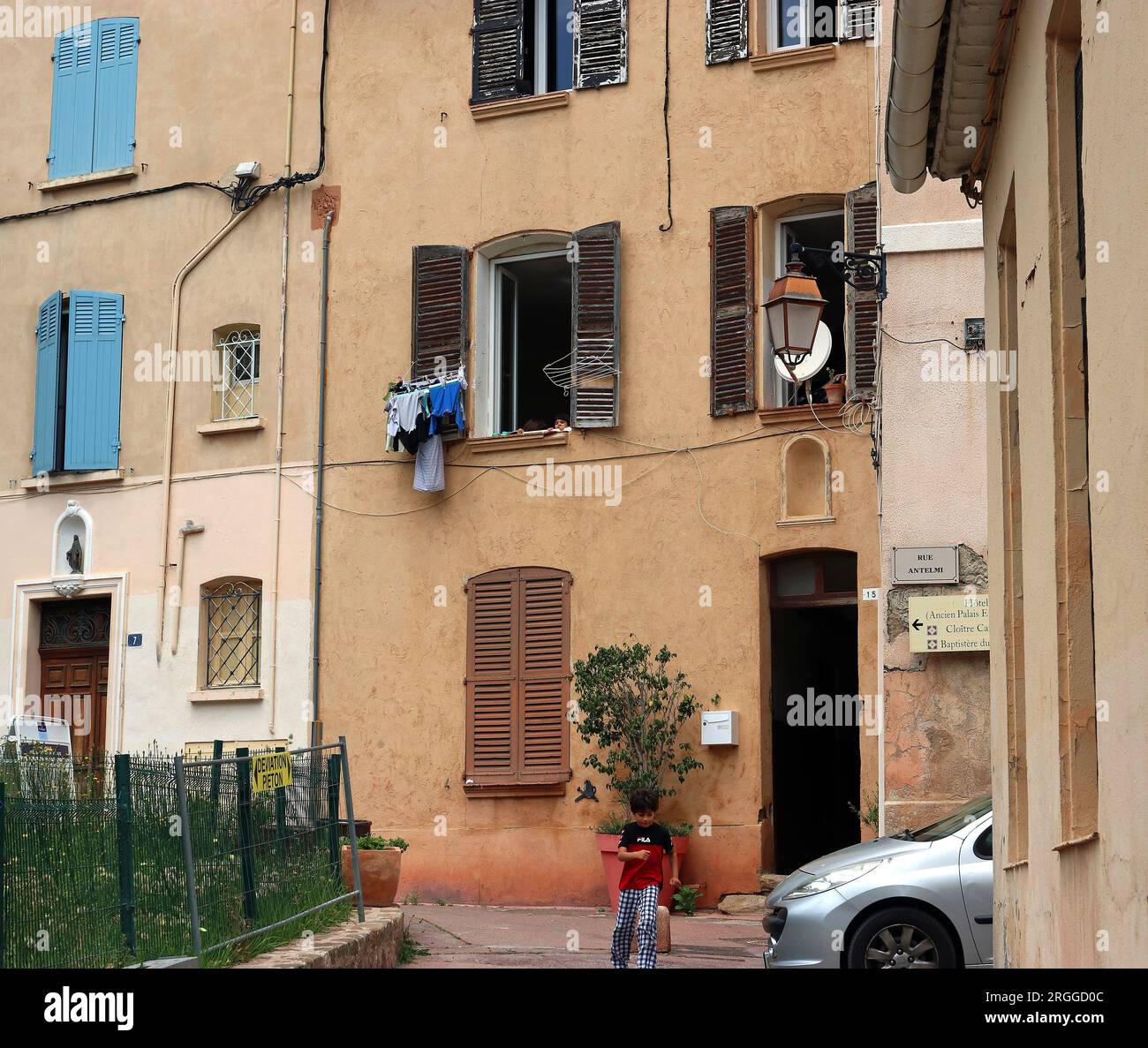 Un ragazzo corre felicemente vicino a casa sua; sua sorella gli guarda giù da una finestra chiusa. Centro storico di Fréjus, villaggio provenzale nel Var, se Francia Foto Stock