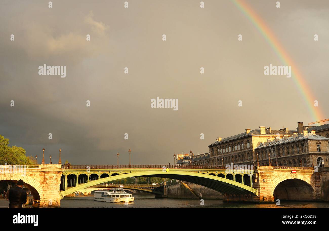 Il metallo verde del Pont Notre Dame, che attraversa la Senna a Parigi, brilla nella luce dorata della prima sera dopo la forte pioggia sotto un debole arcobaleno Foto Stock