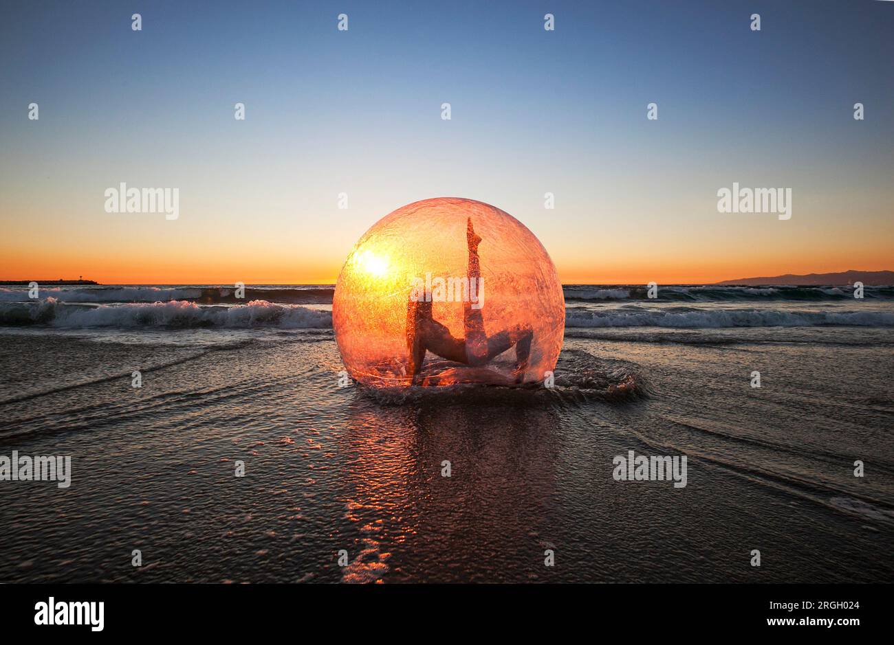 Tramonto con una persona all'interno di una sfera traslucida sulla spiaggia Foto Stock