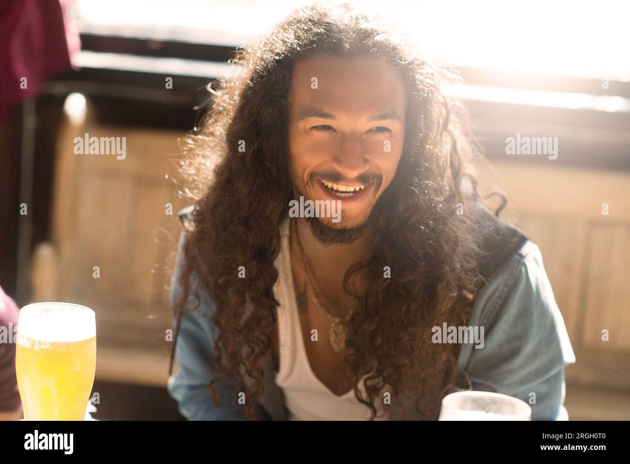 Uomo sorridente con un drink a un tavolo soleggiato Foto Stock