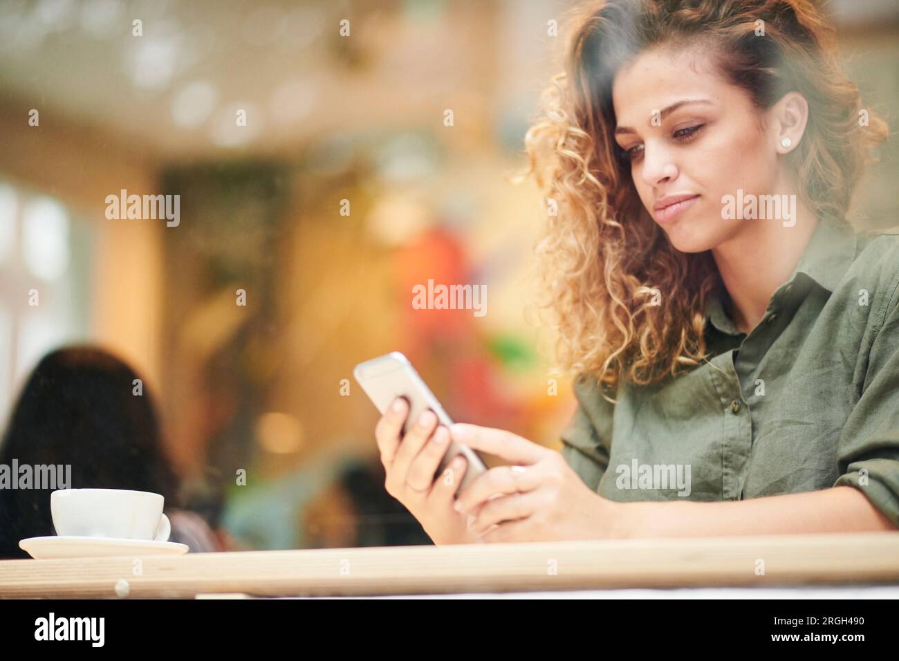 Giovane donna utilizzando smart phone dietro la finestra cafe Foto Stock