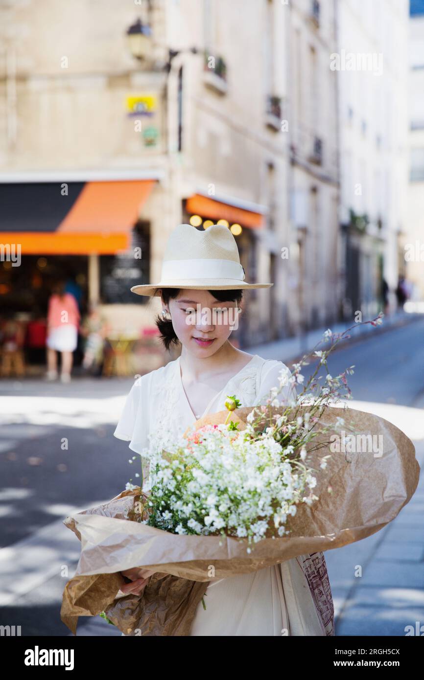 Donna che indossa un cappello di paglia che porta fiori per strada Foto Stock