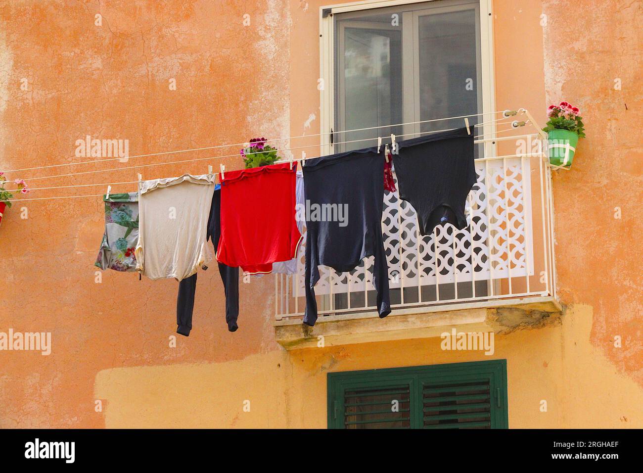 Giornata di lavaggio ad Amalfi, Italia, i vestiti lavati asciugano in una brezza mediterranea su una linea di vestiti allungata tra due balconi, su una facciata colorata. Foto Stock
