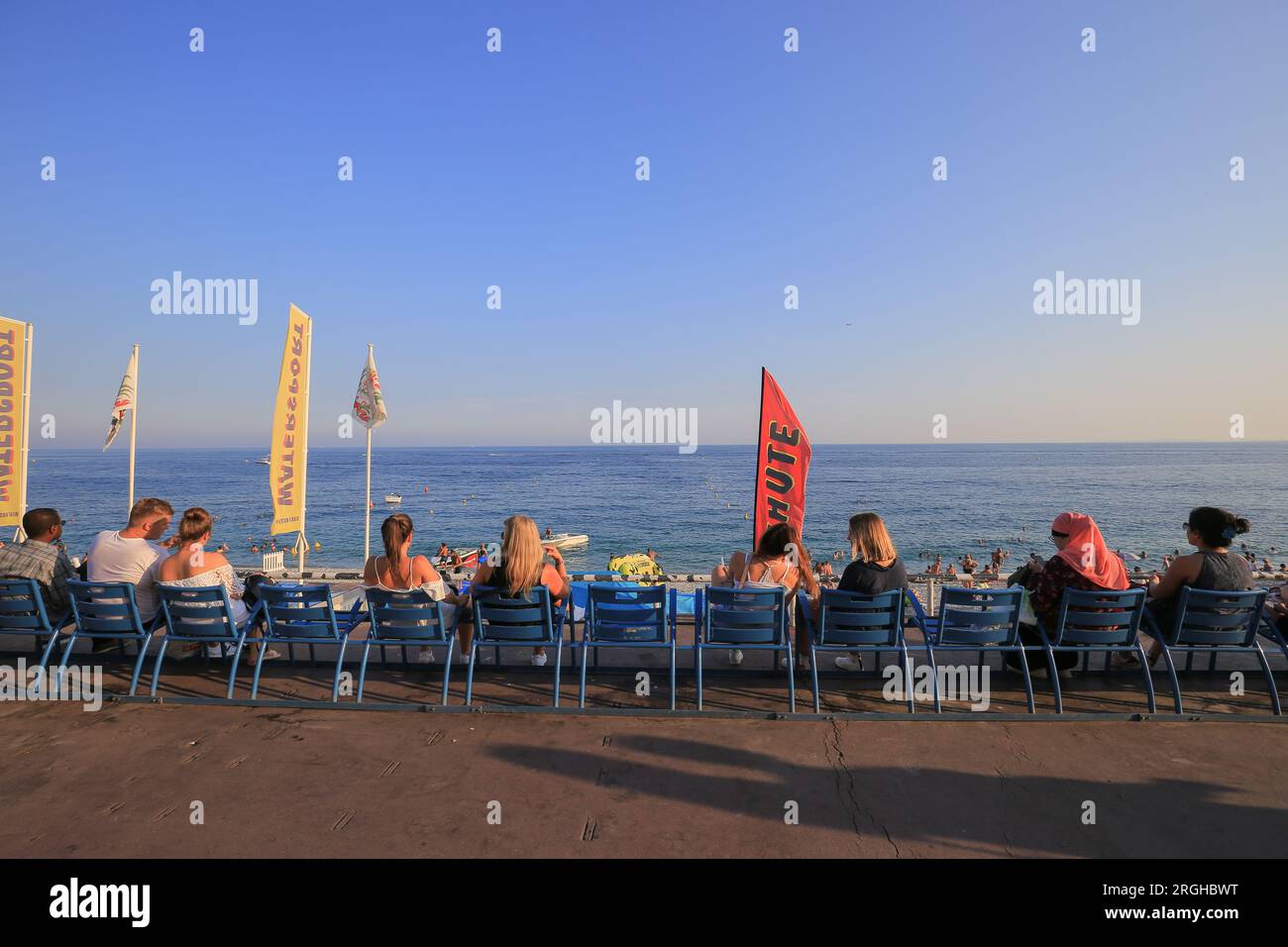 La gente si siede su sedie blu sul lungomare della Costa Azzurra a Nizza Foto Stock