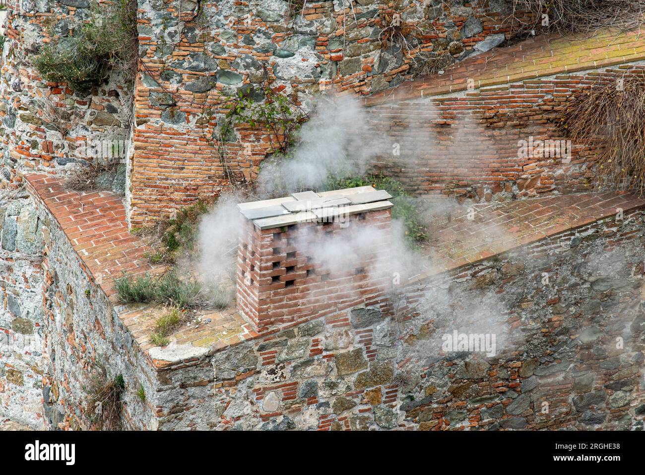 Dettaglio del camino fumante di un antico edificio in mattoni e pietra, Italia Foto Stock