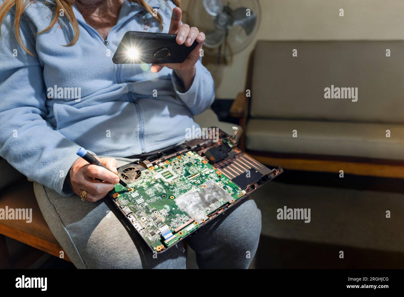 riparazioni di computer, anziana donna degli anni settanta che ripara il suo notebook, tenendo la luce del telefono per vedere meglio Foto Stock