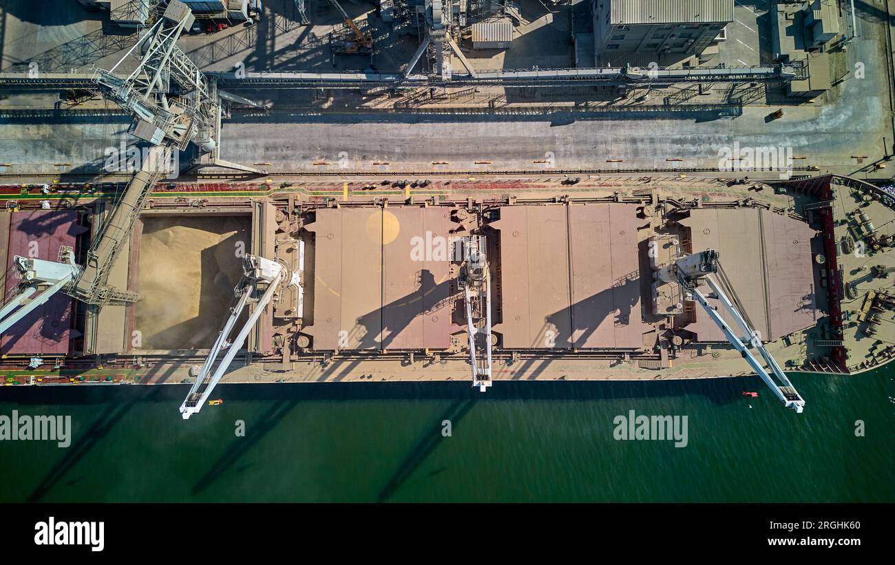 Caricamento del grano nelle stive della nave da carico marittima nel porto marittimo da silos di stoccaggio del grano. Bunkeraggio di nave da carico secco con grano. Vista dall'alto dell'antenna. Foto Stock