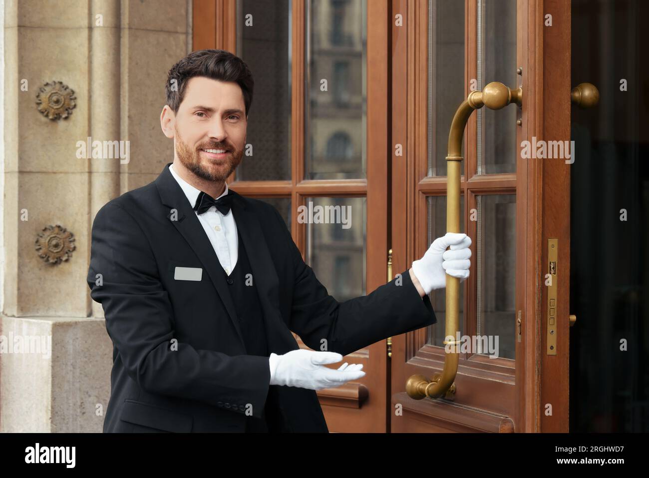 Maggiordomo in elegante abito e guanti bianchi che aprono la porta  dell'hotel in legno Foto stock - Alamy