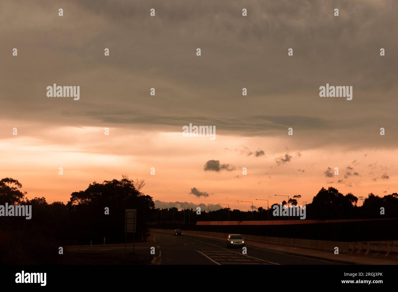 Sotto un tramonto dorato, le auto viaggiano lungo la strada, creando una bella e tranquilla scena. Foto Stock