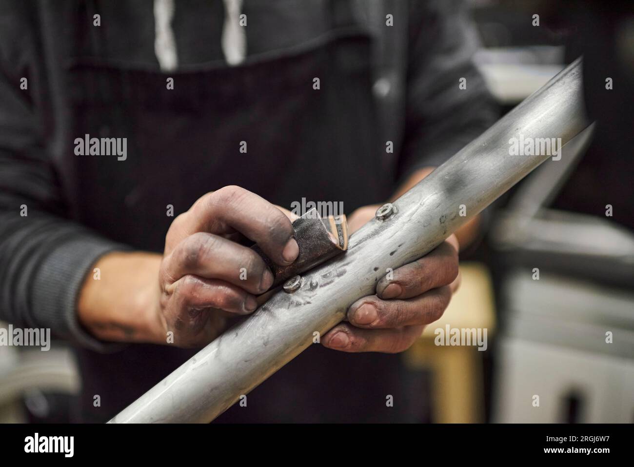 Mani di una persona irriconoscibile che levigano un telaio di bicicletta non verniciato come parte del processo di ristrutturazione di una bicicletta effettuato presso la sua officina. Primo piano c Foto Stock