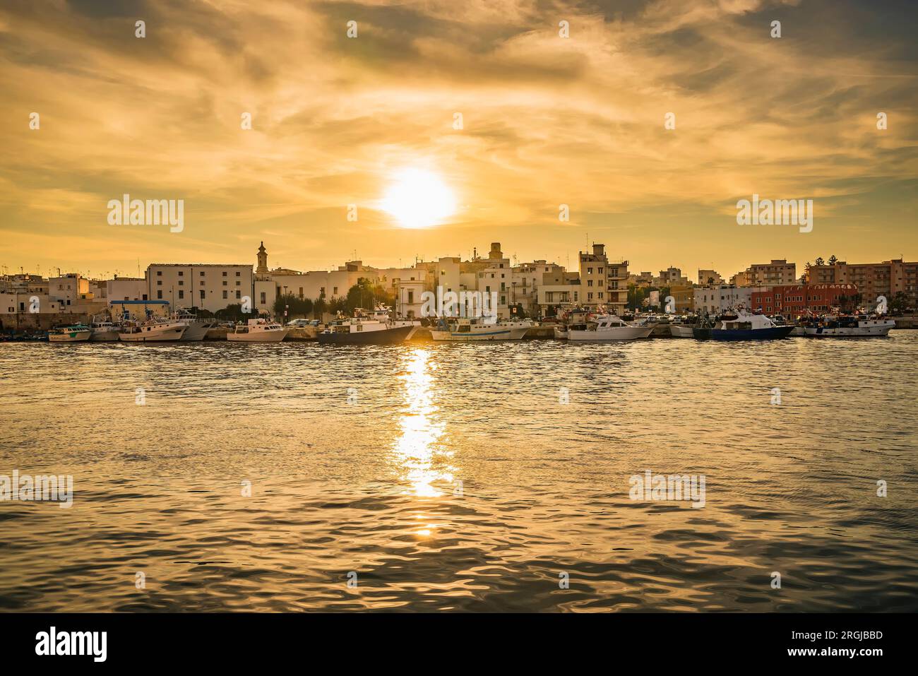 Il riflesso del tramonto luccica e balla sulle dolci increspature dell'acqua sul porto di Monopoli, creando un sentiero di luce scintillante che conduce Foto Stock