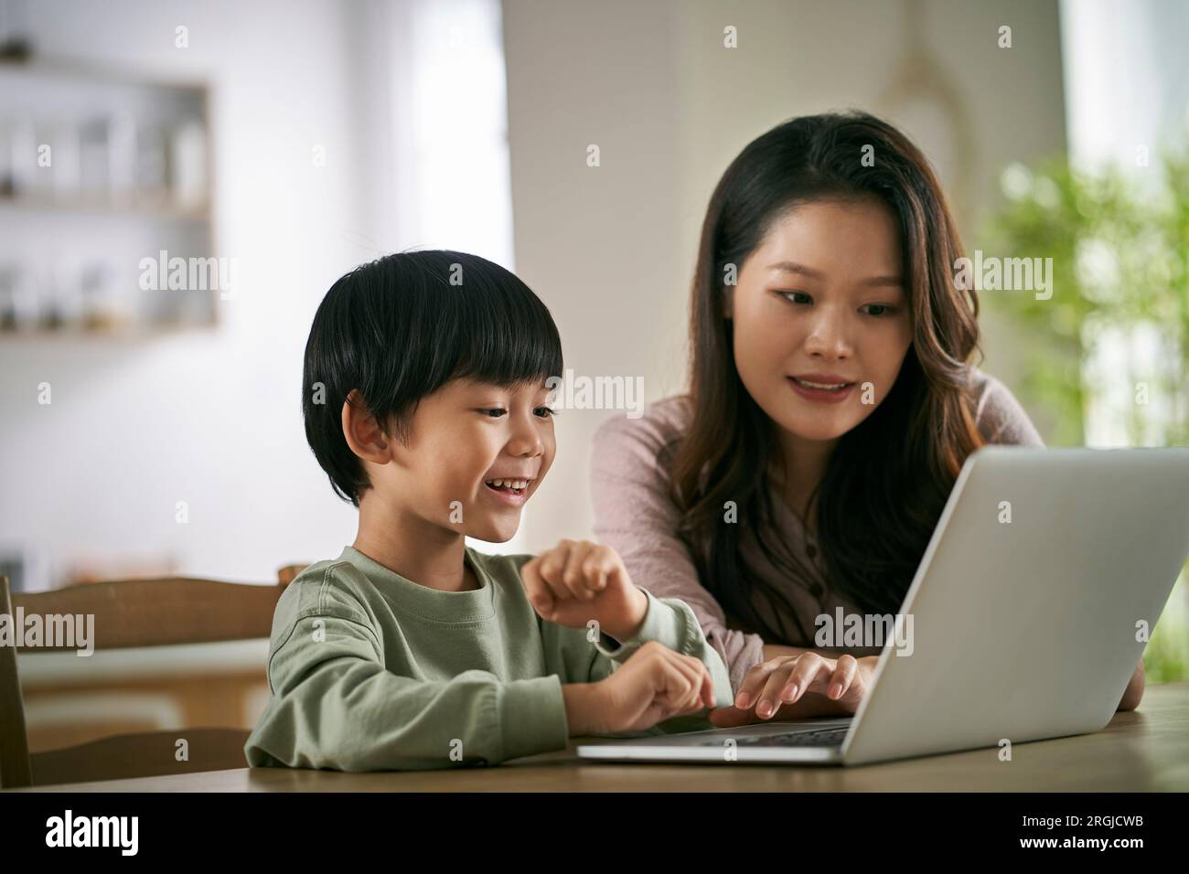 mamma e figlio asiatiche seduti al tavolo a casa a guardare film usando un computer portatile Foto Stock
