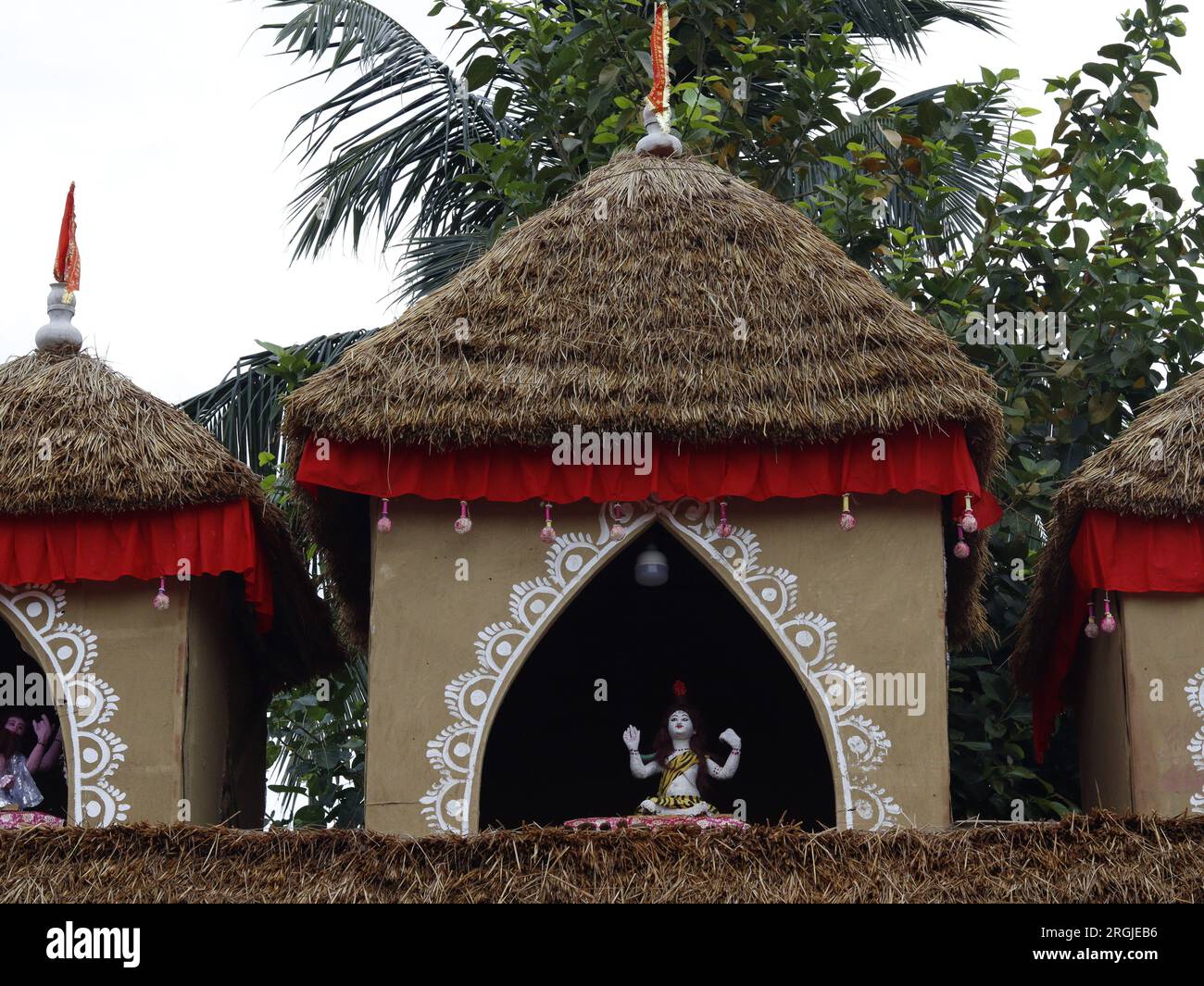 Una capanna indiana chiamata tempio hindu shiv bishnu fatta di fango e legno. Il tetto è fatto di rami. Vegetazione sullo sfondo Foto Stock