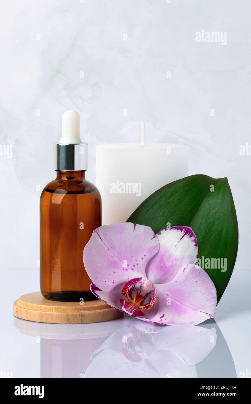 Primo piano della bottiglia di siero in vetro marrone e della candela bianca profumata in bagno. Essenza, olio per massaggi. Fiore d'orchidea. Prodotti di bellezza naturali biologici del centro benessere Foto Stock