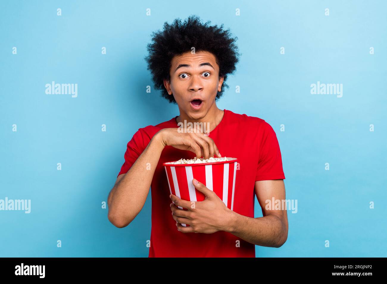 Foto di un giovane ragazzo stravagante, eccitato e scioccato, che guarda un interessante secchio di caramelle di mais isolate su sfondo blu Foto Stock