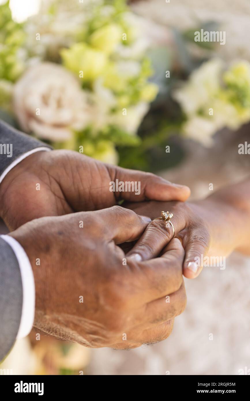 Mani dello sposo birazziale senior che mettono l'anello nuziale al dito della sua sposa Foto Stock